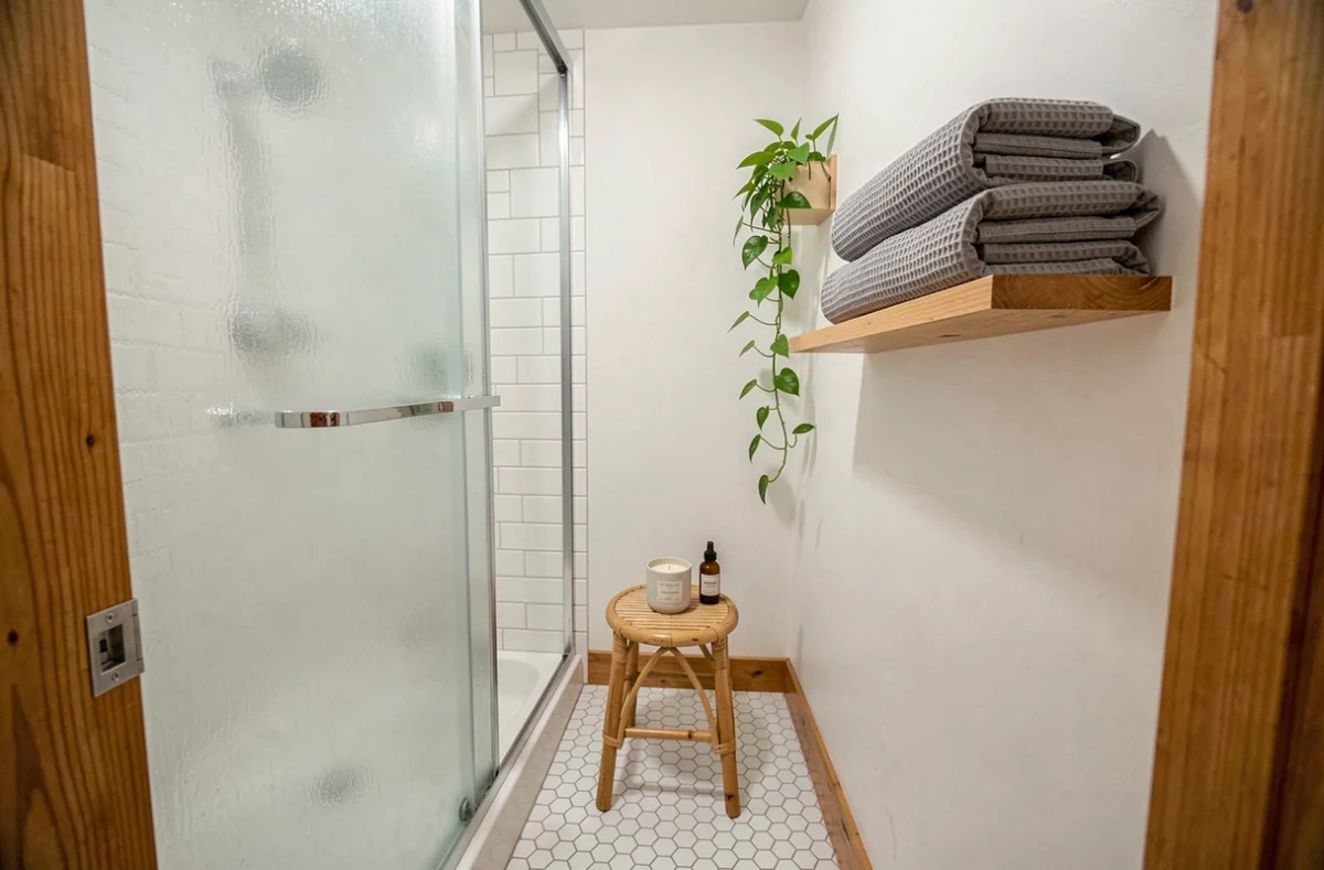 Salle de bains compacte transformée en espace spa avec douche à effet pluie, bougie et plantes vertes